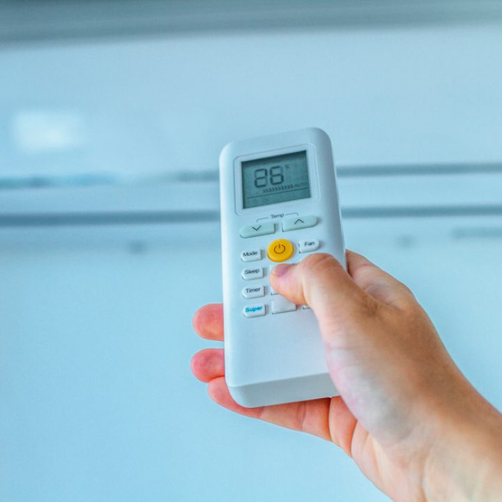 Air conditioner temperature adjustment with remote controller in room at home.